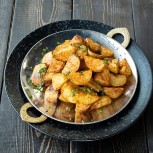 Close-up of crispy seasoned potato wedges garnished with herbs, elegantly served on a decorative plate.