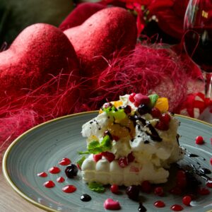 Delicious dessert with fruits and cream served with red wine on a Valentine's themed table.