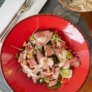 Delicious gourmet salad with roasted meat and nuts on a vibrant red plate, captured indoors.