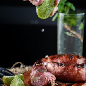 Grilled sausage drizzled with lime juice on a wooden serving board.