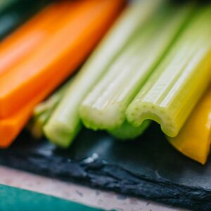 Vibrant mix of fresh carrot, celery, cucumber, and bell pepper sticks on slate board.