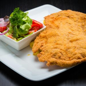 Golden crispy schnitzel served with a fresh vegetable salad, presented on a square plate.