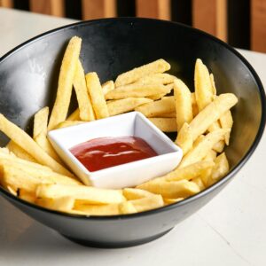 Crispy French fries served with ketchup in a stylish black bowl on a white surface.