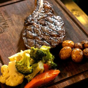 A succulent ribeye steak served with roasted vegetables on a wooden board.