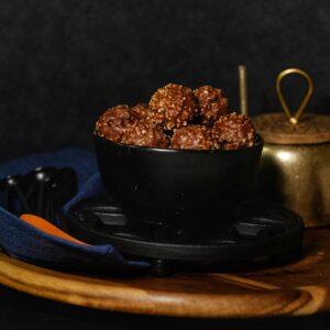 Close-up of chocolate hazelnut truffles in a black bowl with rustic kitchenware background.