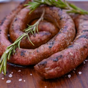 Close-up of a grilled sausage garnished with rosemary, capturing rustic flavors on a wooden board.