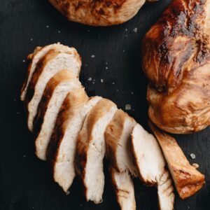 Sliced and whole grilled chicken breasts on a dark slate surface, seasoned perfectly.