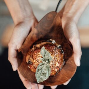 Close-up of hands holding a gourmet stuffed eggplant topped with basil, perfect for culinary presentations.