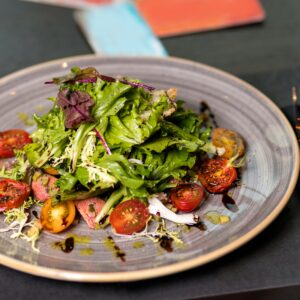 Healthy and vibrant green salad with cherry tomatoes served on a ceramic plate with cutlery.